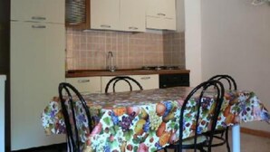 A compact kitchen with white cabinets, a tiled backsplash, and a dining table with a fruit-patterned tablecloth. - TORRE DEI CORSARI, THE PEARL OF THE GREEN COAST - IUN Code: P7053 (Arbus)