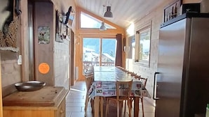 A kitchen with a wooden island, a dining table with chairs, a refrigerator, and a view through the windows.