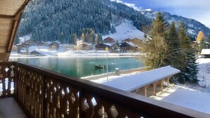 A view from a wooden balcony overlooking a lake with snow-covered houses and mountains in the background. -  380 m² + sauna + 5 fitness passes for Châtel + 15 free multipasses (Châtel)