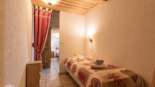 A small, cozy bedroom with a bed, a wooden nightstand, and a red curtain. -  380 m² + sauna + 5 fitness passes for Châtel + 15 free multipasses (Châtel)