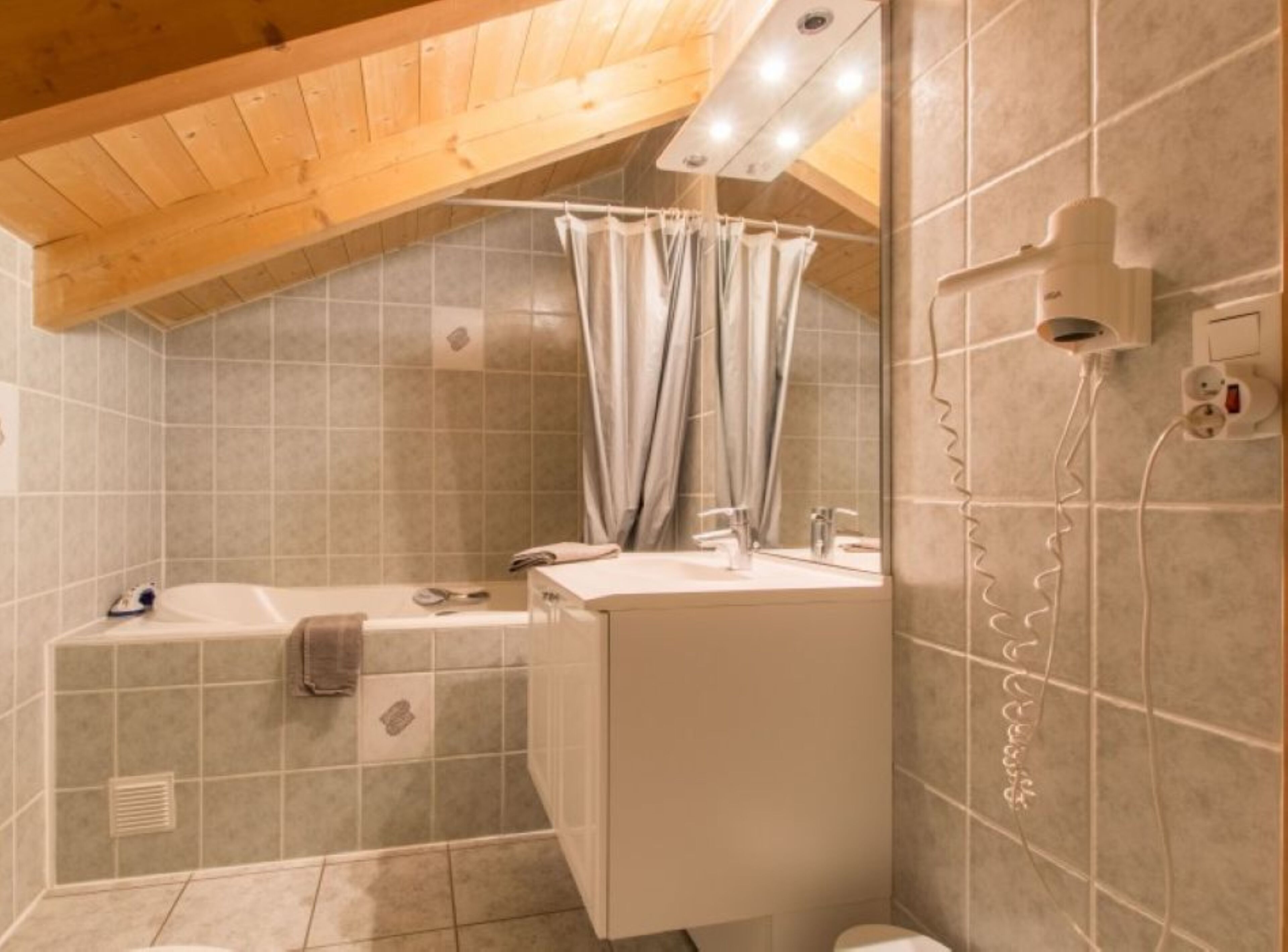 A small, cozy bathroom with a sloped ceiling, a bathtub, a vanity with a mirror, and a shower curtain.