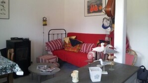 A cozy room with a red sofa, a small round table, and a hanging guitar. - The Port of Millstone, island of Yeu, house with garden pets allowed (L'île-D'yeu)