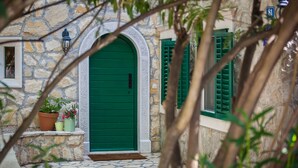 A stone building with a green door and shutters, potted plants, and a stone pathway.