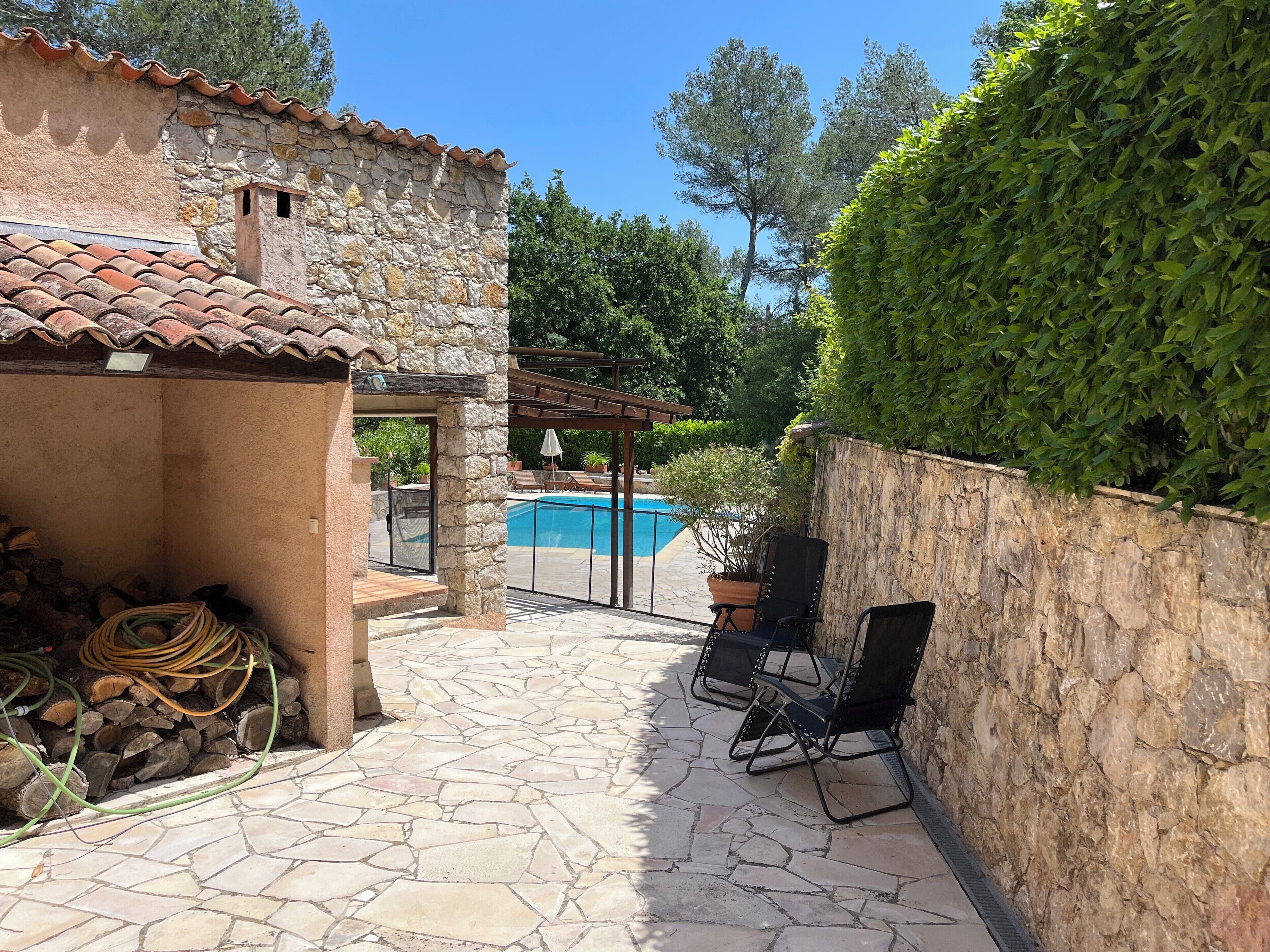 Un bâtiment en pierre avec un toit en tuiles, une piscine et un espace extérieur aménagé pour s’asseoir.