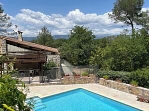 A pool area with a stone deck, a wooden pergola, and a stone building with a tiled roof. - Beautiful villa in in Provence with Large 5x10 pool, gardens, for 10 guests (Saint-Paul-En-Forêt)