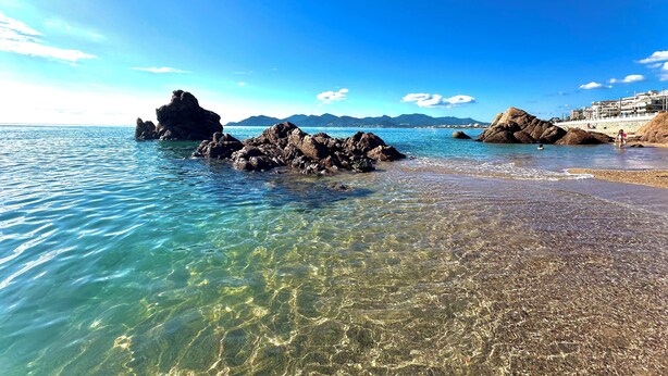 A coastal beach with clear water, rocky formations, and distant mountains. - Cannes - Sea front apartment, beach front, pool, garden, internet, aircon (Cannes)
