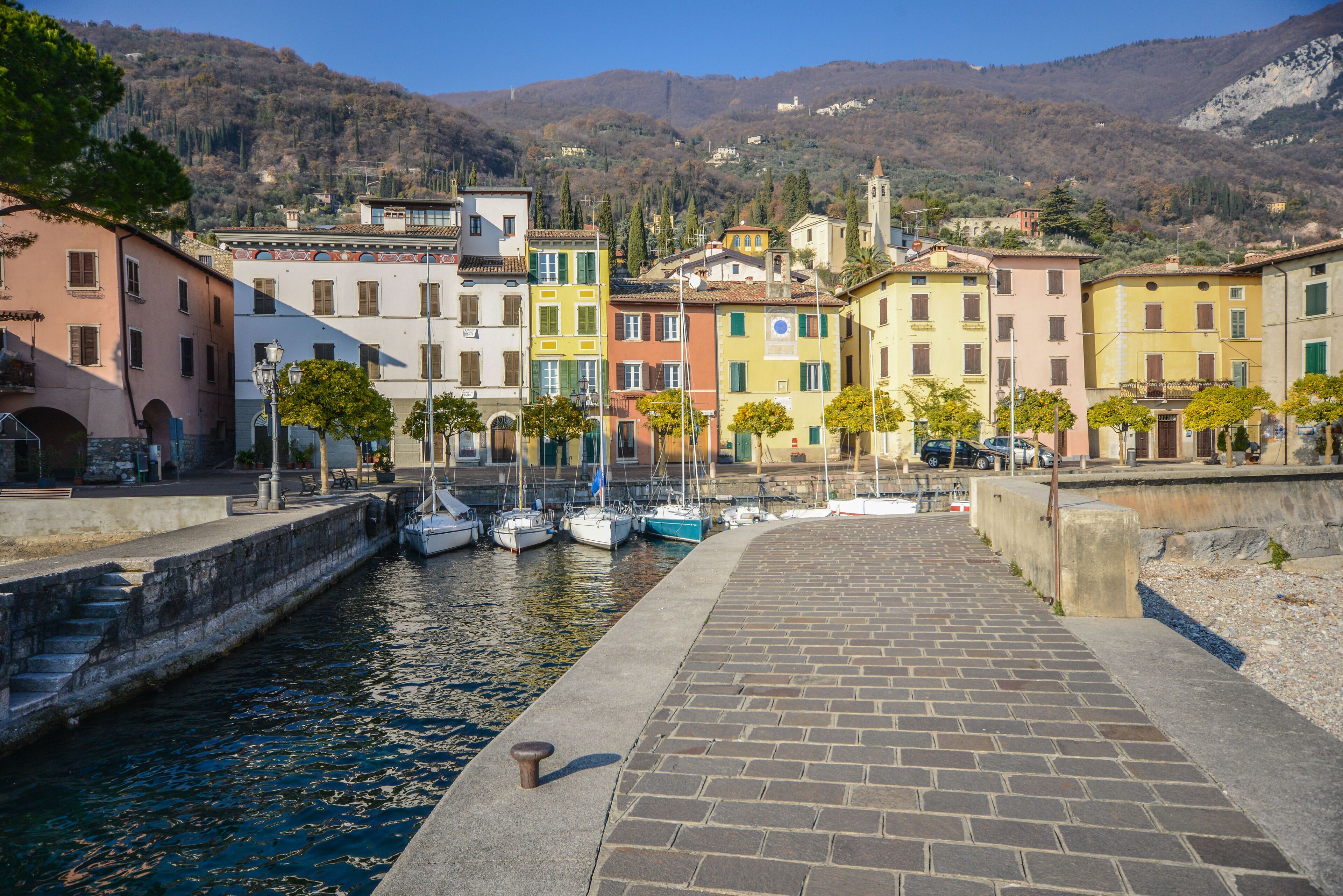 Une promenade en bord de mer bordée de bâtiments aux couleurs vives, un canal étroit et des bateaux amarrés.