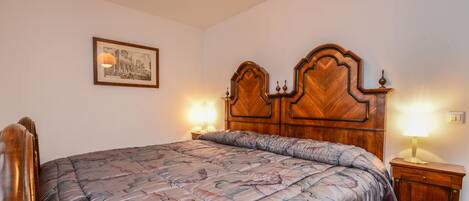 A neatly made bed with a floral-patterned bedspread, a wooden headboard with decorative carvings, and two bedside lamps.