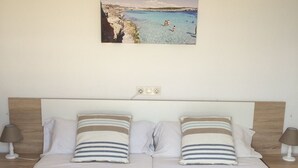 Ein Doppelbett mit zwei Kissen, ein Kopfteil mit einer Holzvertäfelung, ein an der Wand befestigtes Bild von einem Strand und Nachttischlampen.
