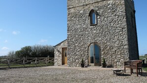 A stone tower with a wooden door and arched windows, surrounded by a gravel area with a wooden fence and benches. - Listed Stone Built Folly with original gothic features (Seaham)