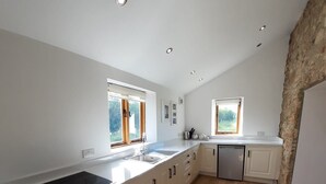 A modern kitchen with white cabinetry, a wooden countertop, and a built-in oven. There are two windows providing natural light, and the floor is made of light-colored wood. - Listed Stone Built Folly with original gothic features (Seaham)