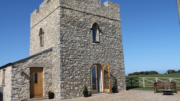 A stone building with a wooden door and arched windows, a bench, and a fence in the background. - Listed Stone Built Folly with original gothic features (Seaham)