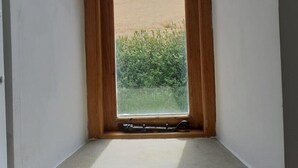 A narrow arched window with a wooden frame, leading to a view of a flat landscape with distant hills and a clear sky. - Listed Stone Built Folly with original gothic features (Seaham)
