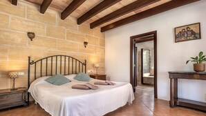 A bedroom with a stone wall, a bed with a white bedspread, two bedside lamps, and a wooden nightstand. - CALA D'OR STUNNING PRIVATE VILLA + BUNGALOW 10 MIN WALK TO BEACH! (Cala d'or)