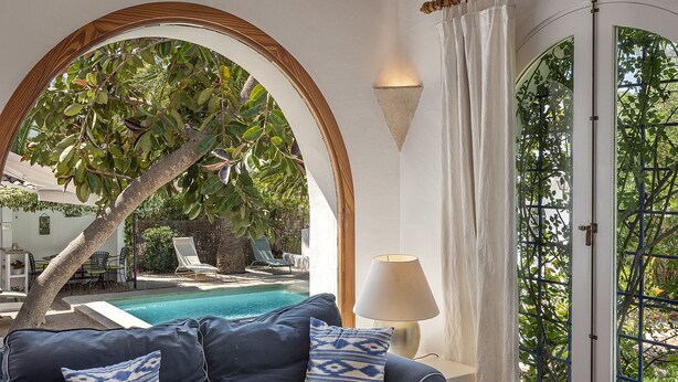 A room with a pool, a sofa with patterned cushions, a lamp, and a view of a tree and outdoor seating area. - CALA D'OR STUNNING PRIVATE VILLA + BUNGALOW 10 MIN WALK TO BEACH! (Cala d'or)