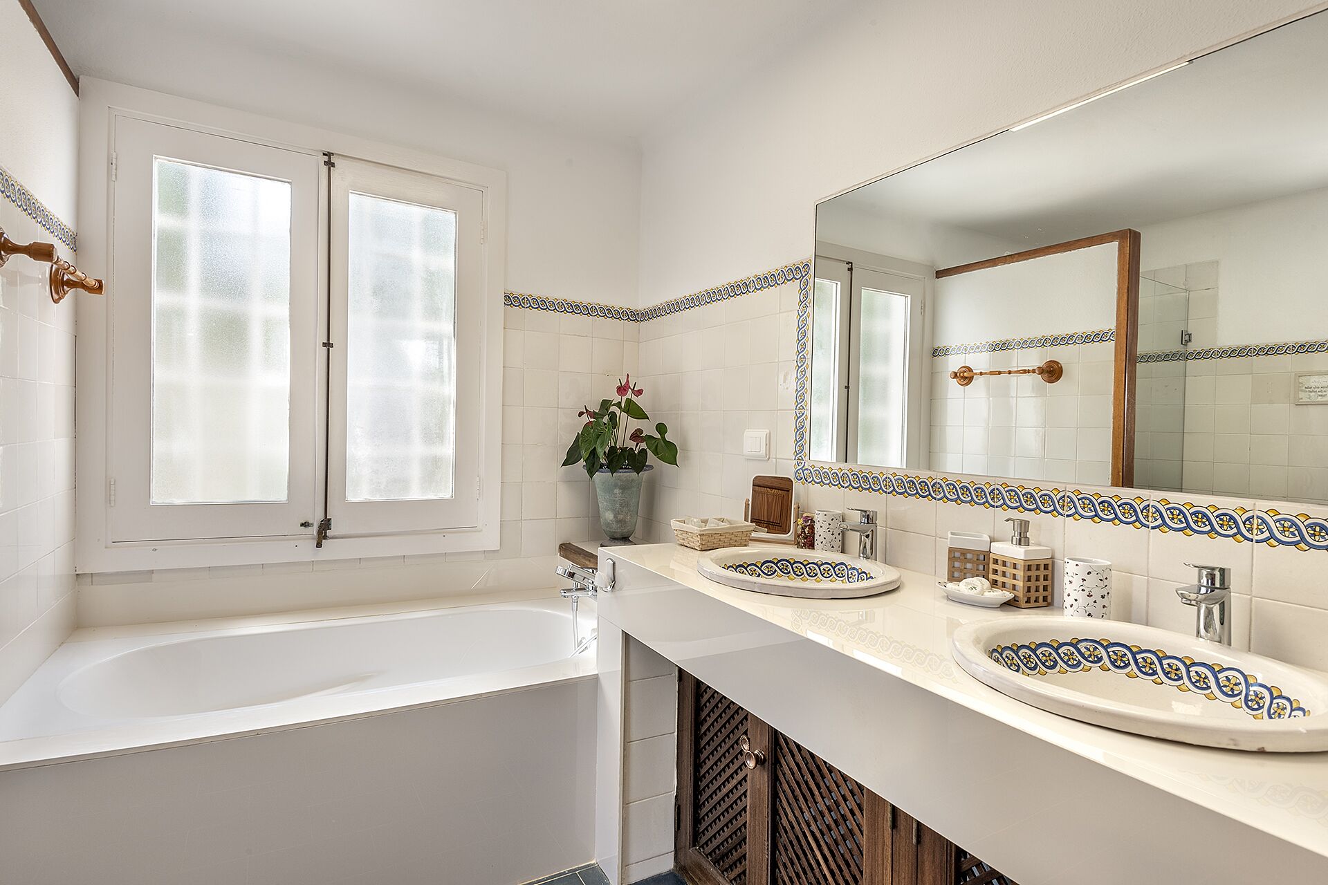 A bathroom with a bathtub, two sinks, a large mirror, and a potted plant.
