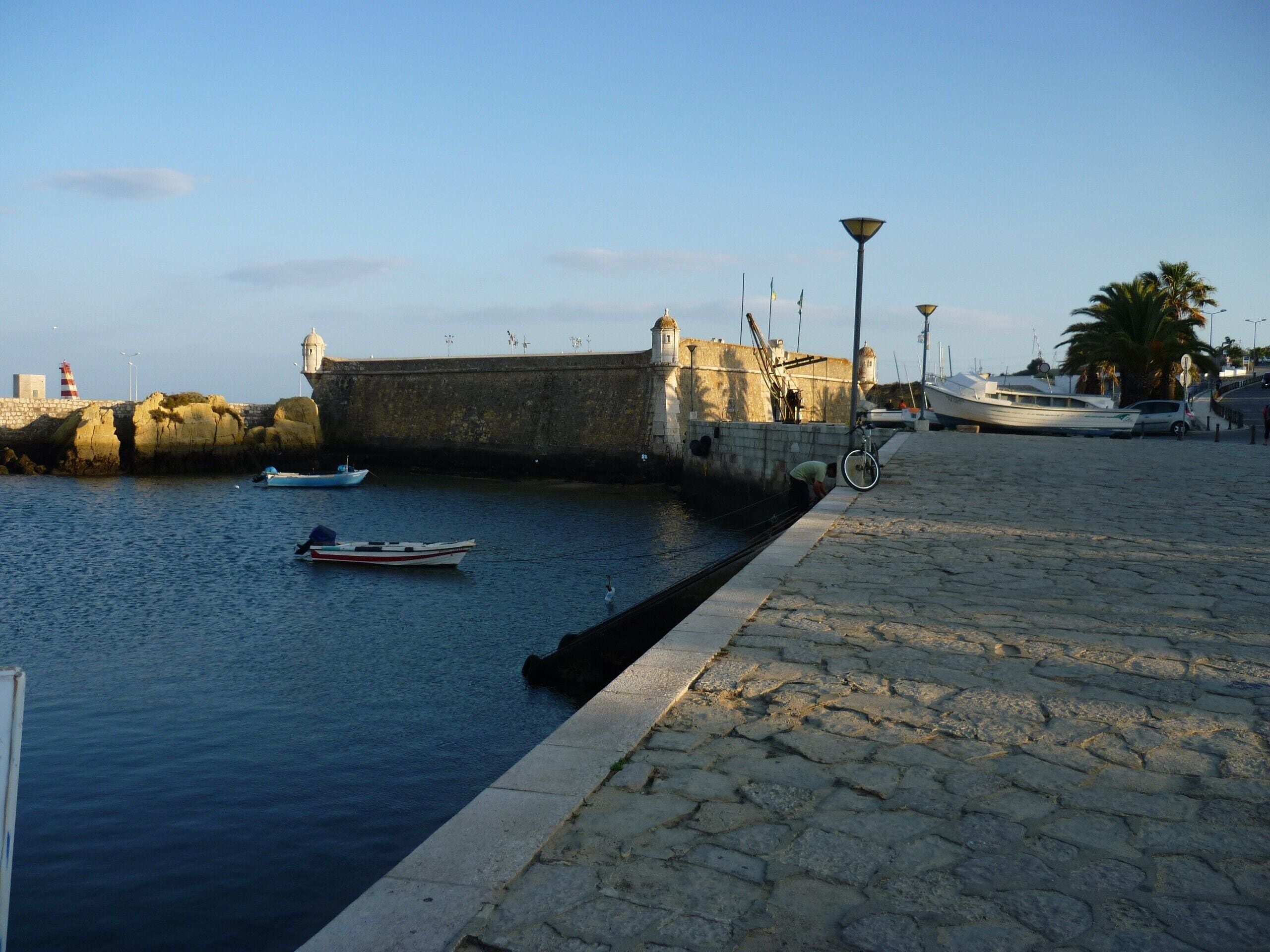 A waterfront promenade with a stone wall, a small boat, and a bicycle.
