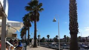 A coastal outdoor dining area with palm trees, a marina in the background, and a café with outdoor seating. - Luxury 2 Bed Apartment with pool near to beach (Porto De Mos)