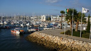 A marina with numerous boats docked, a stone wall, and a flag on a flagpole. - Luxury 2 Bed Apartment with pool near to beach (Porto De Mos)