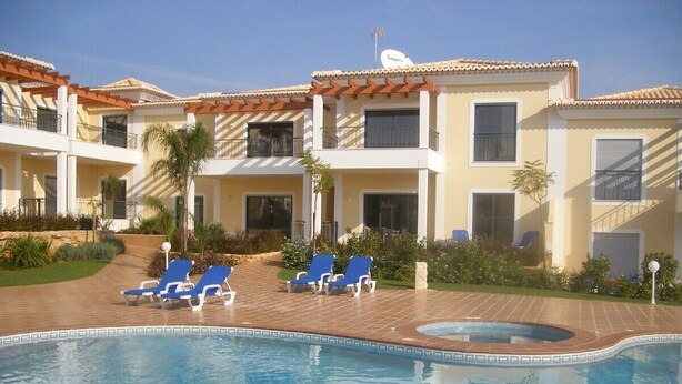 A swimming pool with blue lounge chairs, a hot tub, and a building with balconies and a tiled roof. - Luxury 2 Bed Apartment with pool near to beach (Porto De Mos)