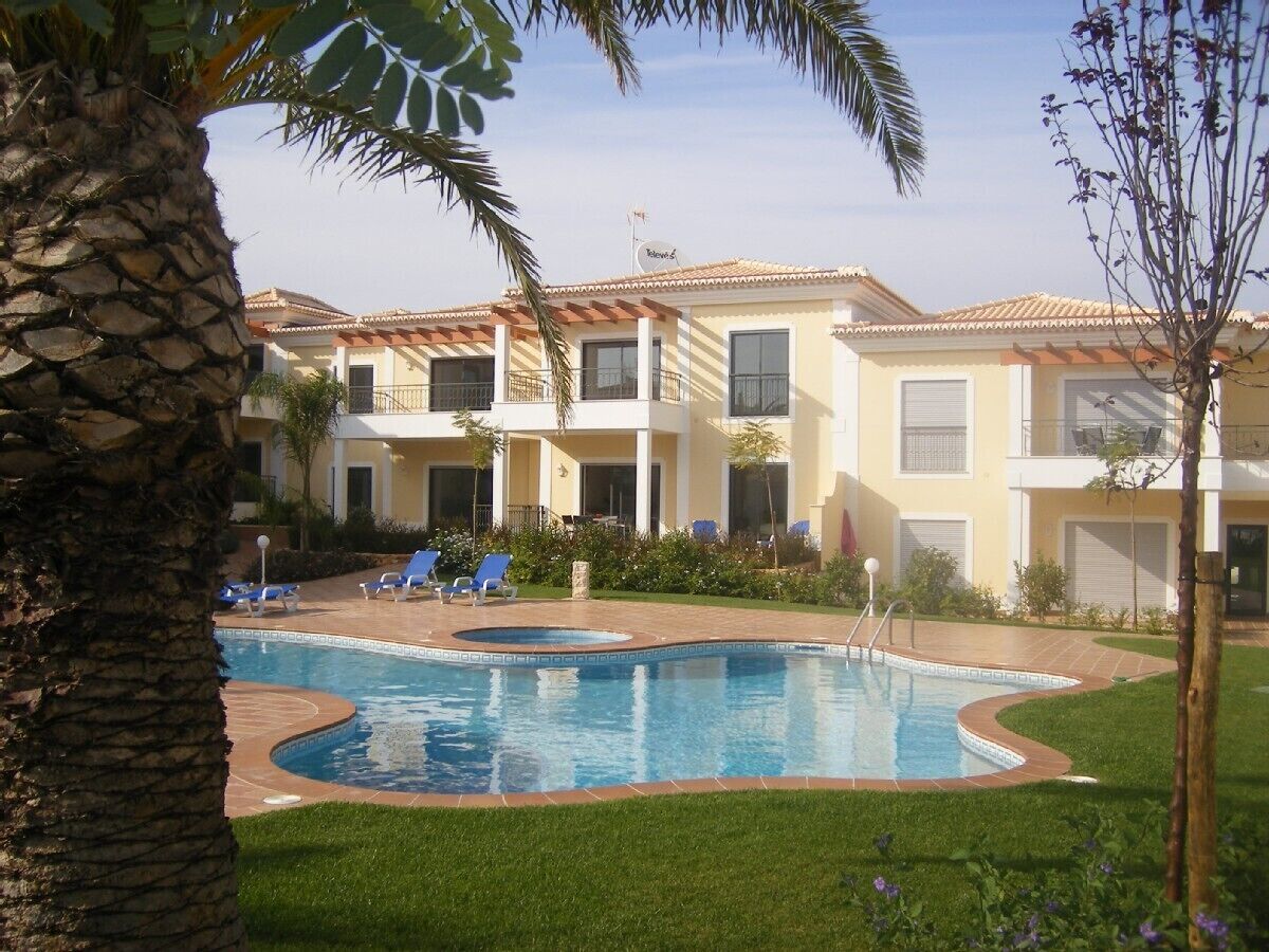A swimming pool with lounge chairs, a palm tree, and a building with a tiled roof.