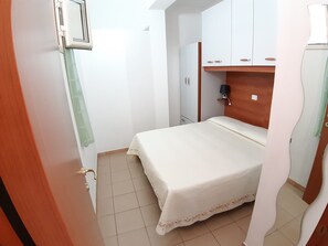 Quarto pequeno e bem organizado, com uma cama, um guarda-roupa e uma mesa de cabeceira.