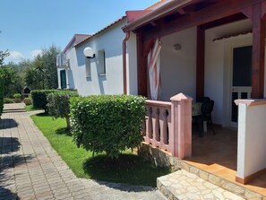Uma casa com varanda coberta, um pequeno jardim e uma porta que dá para um quarto.