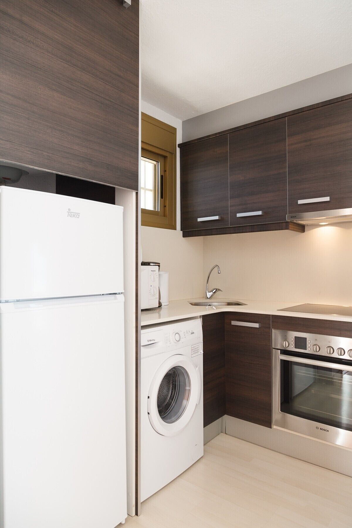 A compact kitchen with a Bosch oven, a washing machine, and a refrigerator.