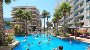 En swimmingpool omgiven av palmer och en flervåningsbyggnad med balkonger.