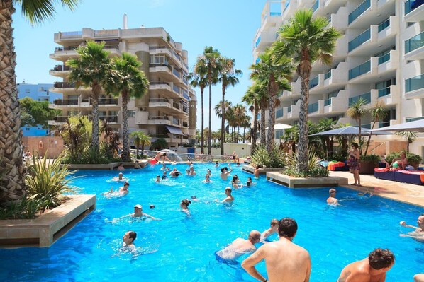 A swimming pool surrounded by palm trees and a multi-story building with balconies.
