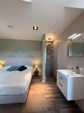 A bedroom with a bed, bedside lamp, and a bathroom with a sink and shower.