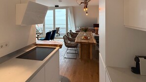 Cozinha moderna com ilha central, área de refeições com cadeiras e vista através de grandes janelas.