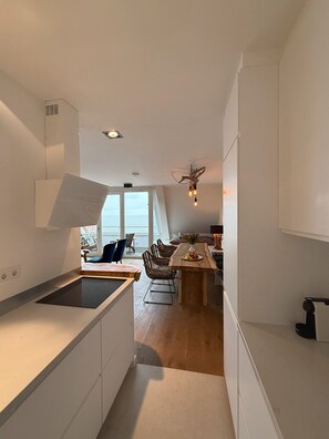A modern kitchen with a central island, dining area with chairs, and a view through large windows.