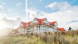 Um hotel de vários andares com telhados vermelhos e paredes brancas, situado perto de uma praia com gramíneas altas.