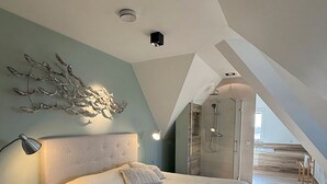 Quarto com uma cama grande, mesa de cabeceira, luminária na parede e luz de teto.