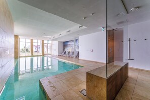 An indoor swimming pool with clear glass walls, a tiled floor, and a view of the outside.