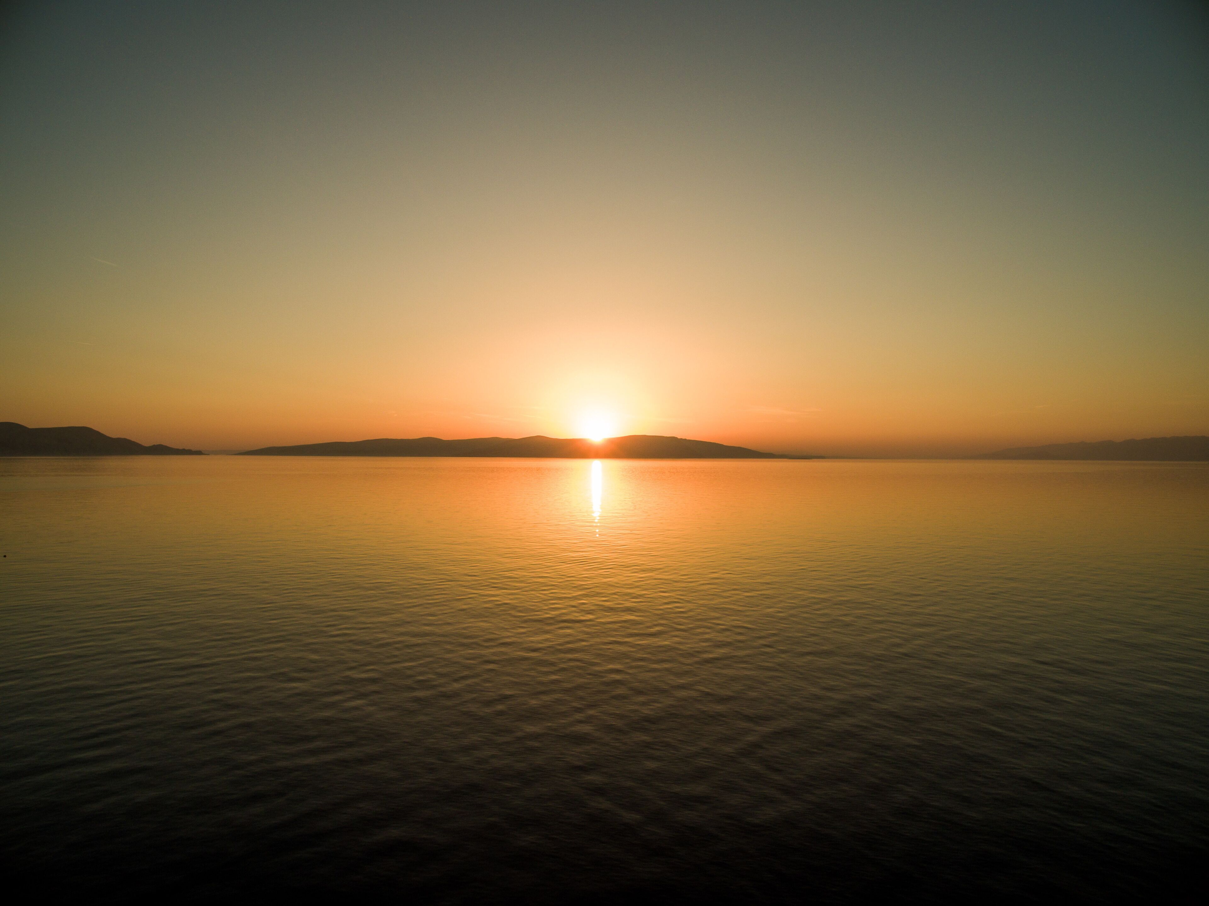 Una masa de agua tranquila reflejando el sol al atardecer.