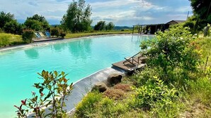 Una piscina con cubierta de madera y sillas de descanso, rodeada de vegetación y árboles.