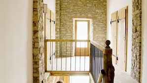 Una escalera con paredes de piedra y vigas de madera que lleva a una habitación luminosa con un ventanal.
