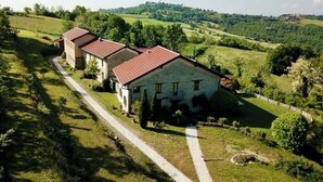 Una hilera de edificios de piedra con tejados rojos, rodeada de campos verdes y árboles, lo que indica un entorno rural.