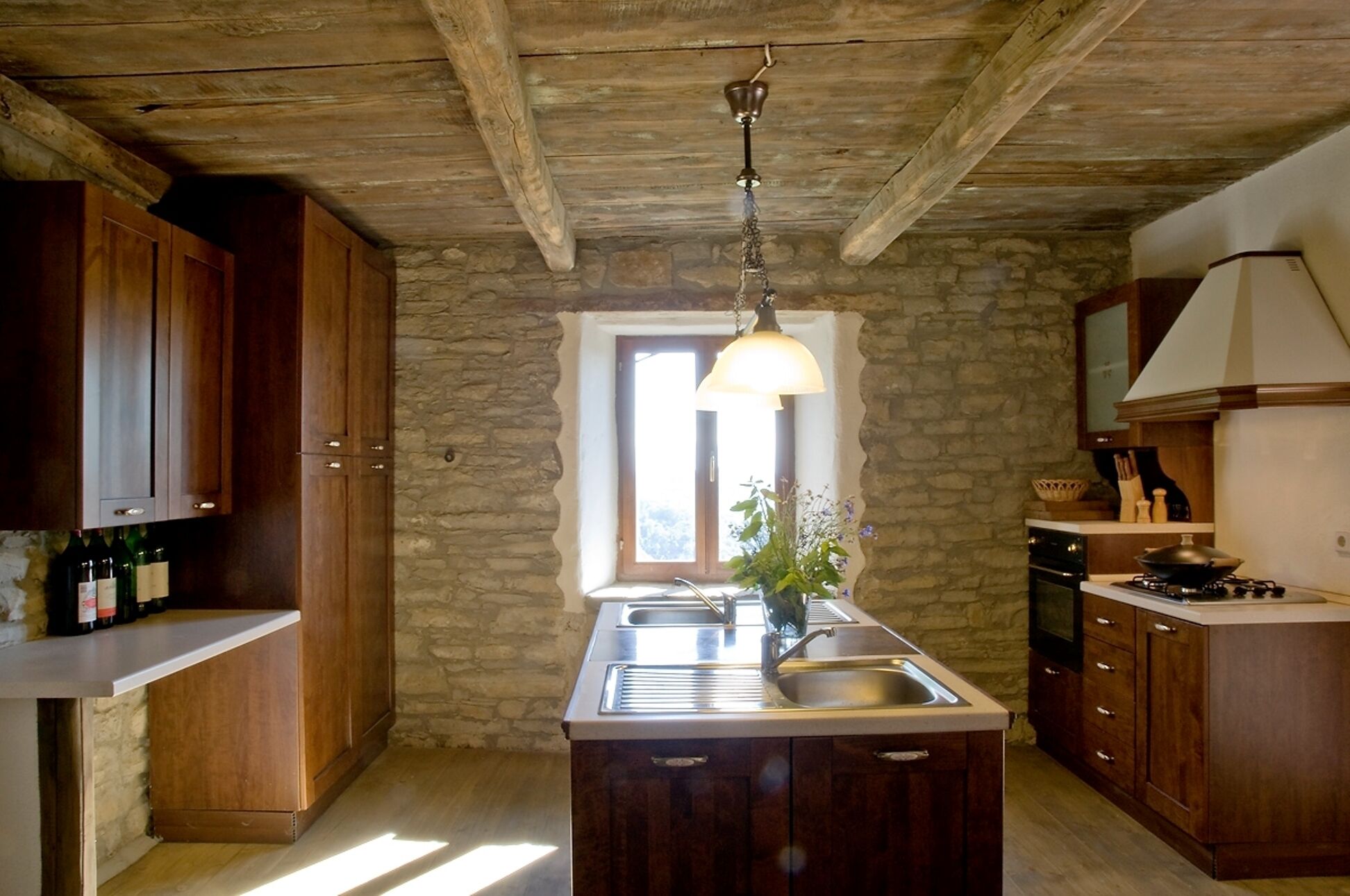 Une cuisine rustique avec des armoires en bois, un mur en pierre, un luminaire suspendu et une fenêtre.