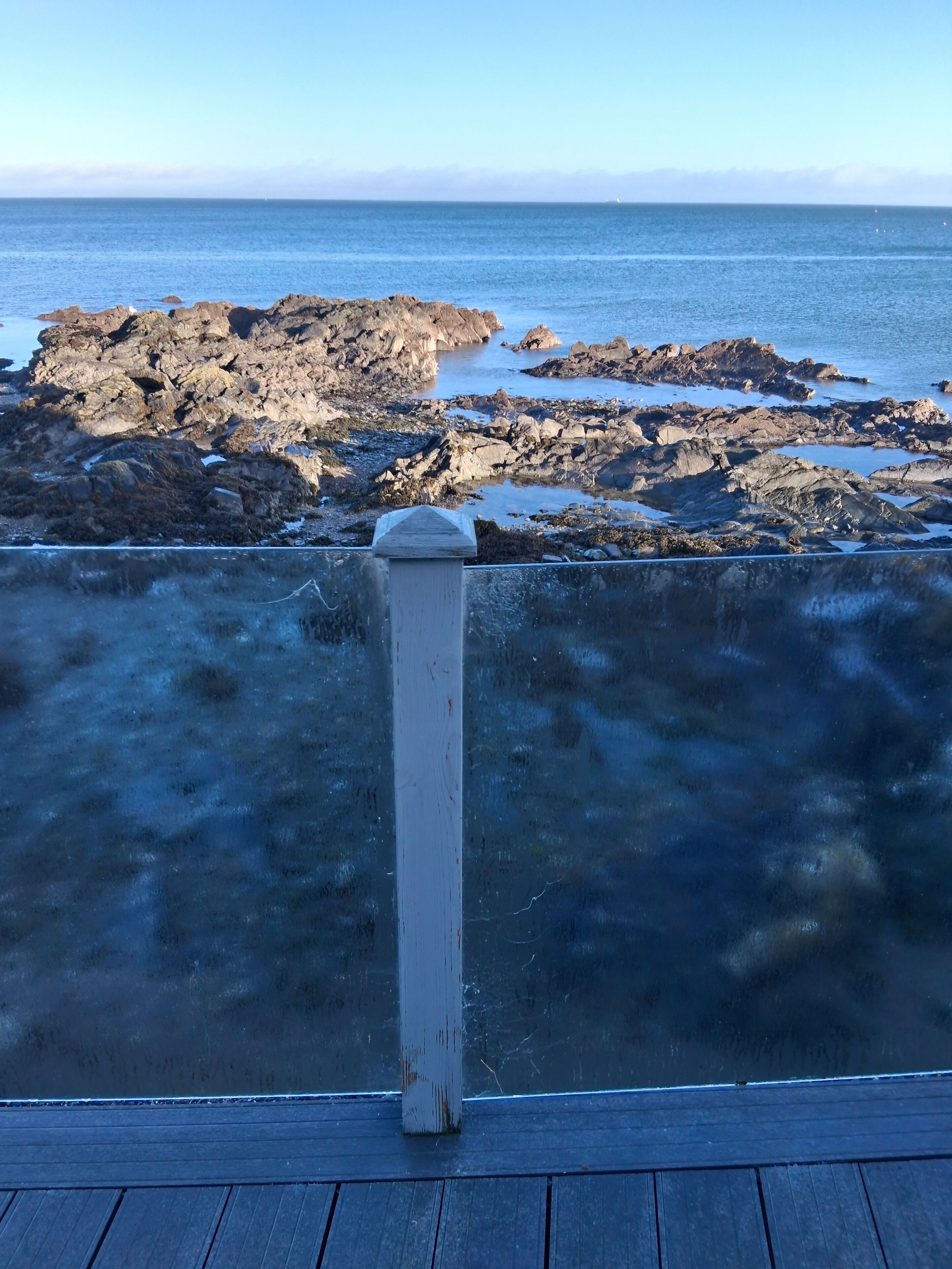 A wooden deck overlooking a rocky shoreline with the ocean in the background.