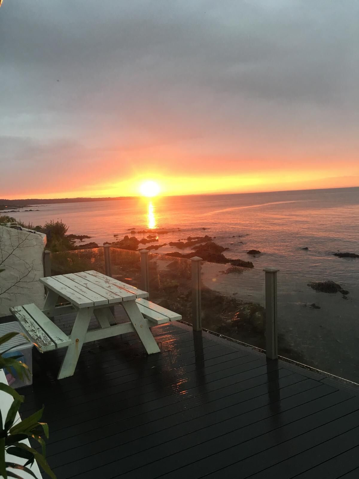 A wooden deck with a picnic table overlooking a sunset over the ocean.