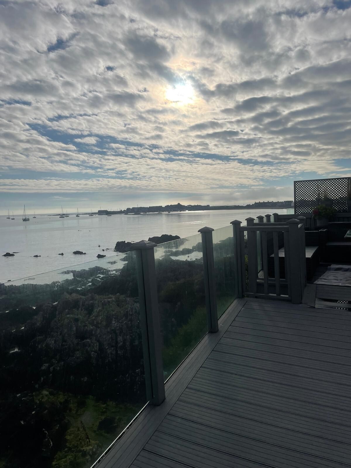 A coastal view from a balcony with a railing, overlooking a calm sea with boats and a distant shoreline.