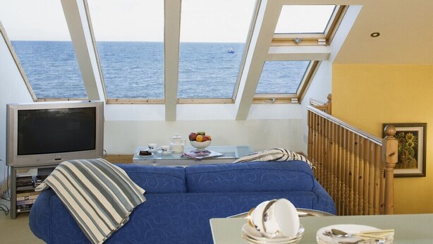 A room with a large window overlooking the sea, a sofa, a television, and a table with a bowl of fruit and tea set.