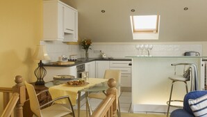 A compact kitchen with white cabinets, a dining table with chairs, a bar stool, and a small window above the sink.