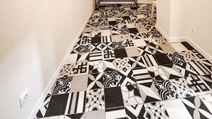A hallway with patterned black and white tiles, a black console table with a plant, and a woven light fixture. - Charming house in downtown Olhão (Olhão)