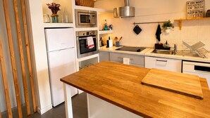 A modern kitchen with white cabinetry, a wooden island, stainless steel appliances, and a unique pendant light. - Charming house in downtown Olhão (Olhão)