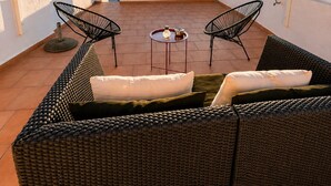 A rooftop patio with a woven ceiling, two black wire chairs, a wicker sofa with cushions, and a small round table. - Charming house in downtown Olhão (Olhão)