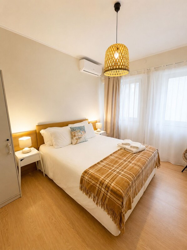 A hotel room with a bed, bedside tables, a lamp, an air conditioner, and a window with curtains. - Charming house in downtown Olhão (Olhão)